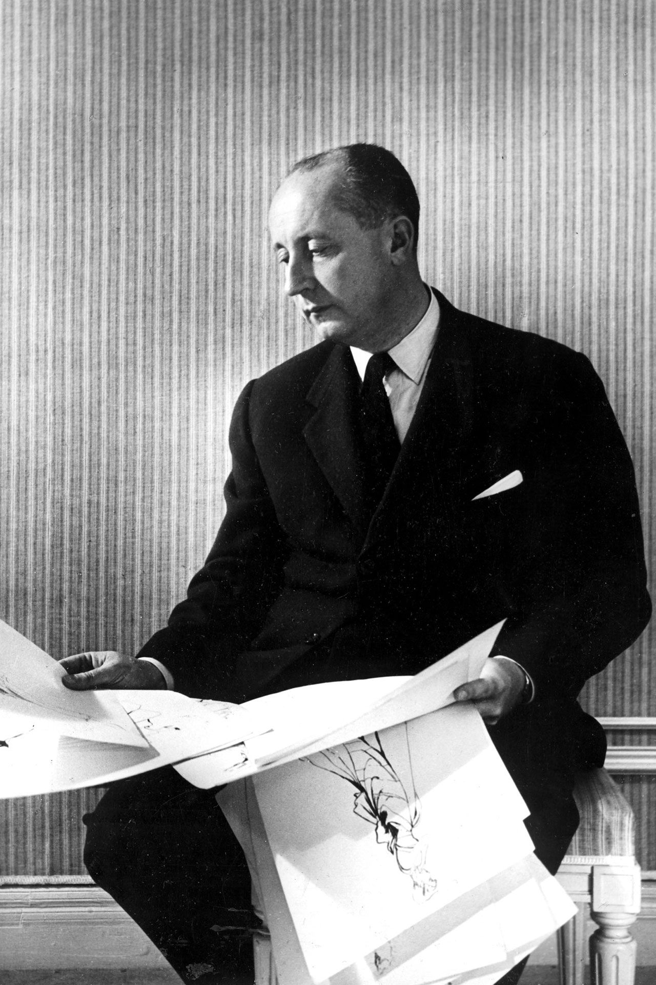 Photo of Christian Dior looking at design drafts.